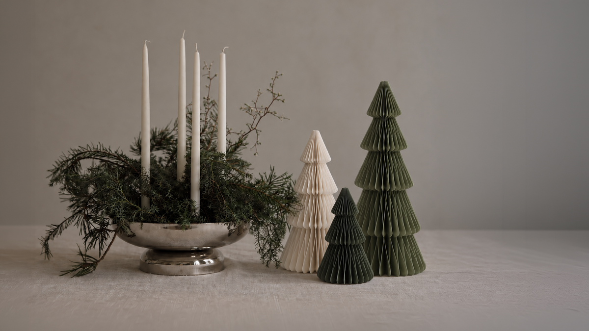 Papier-Weihnachtsbäume in Weiß und Moosgrün neben einem Adventsgesteck mit weißen Kerzen